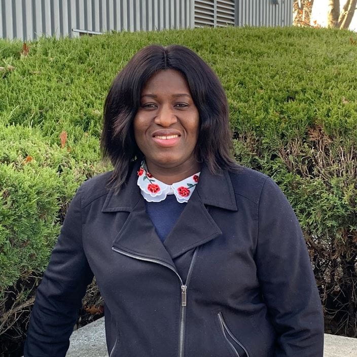 Person in front of green bushes wearing a dark jacket and floral-collared shirt.
