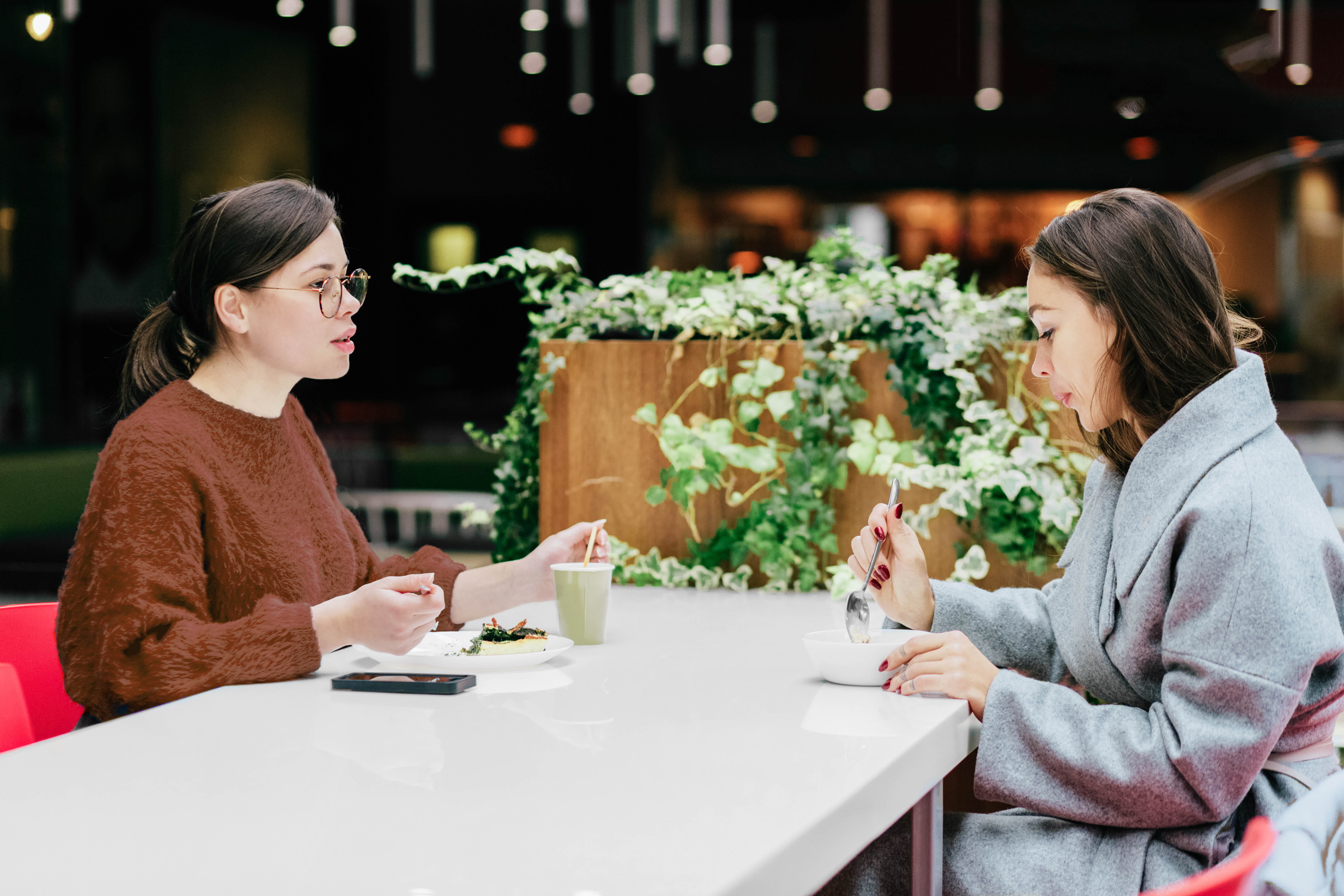 Two young women seated at a table sharing a meal and conversing.
