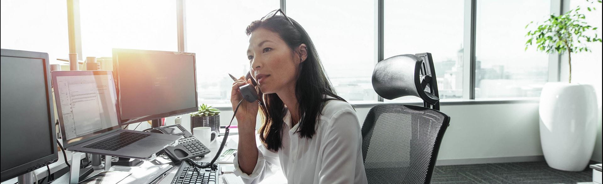 A woman at a desk, talking on the phone with a laptop and papers in front of her.
