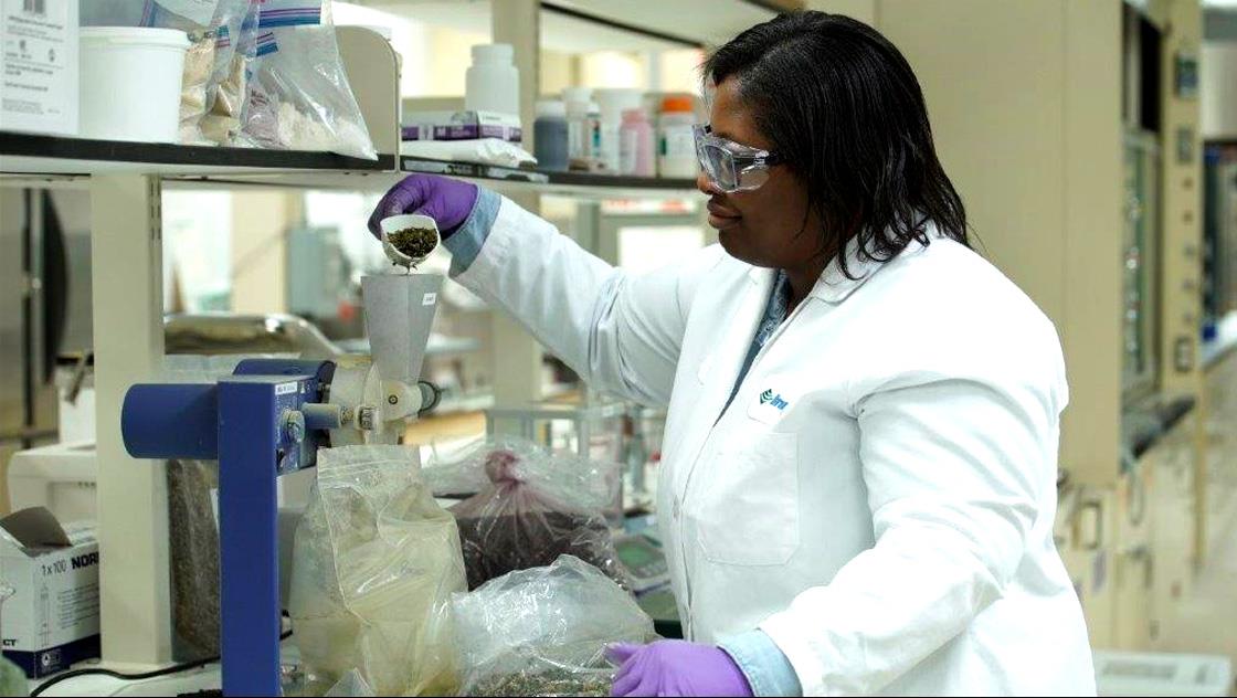 Scientist in a lab coat and gloves working with containers in a laboratory.