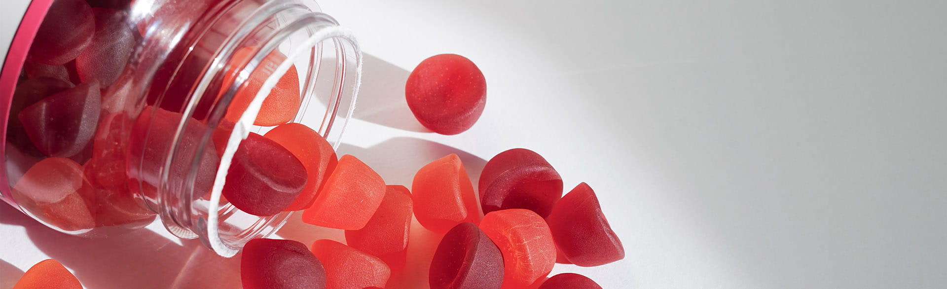 Spilled red gummy vitamins from a jar on a white surface.