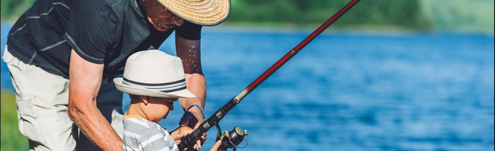Photo of a grandfather teaching his young grandson to fish at a lake.