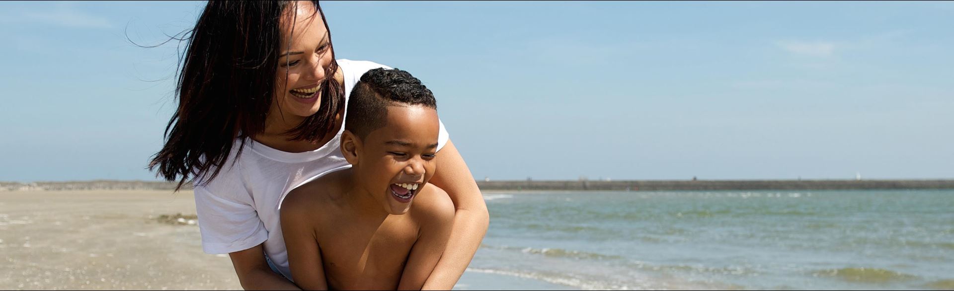 Photo of a mother and son enjoying a day at the beach and playing by the water's edge.