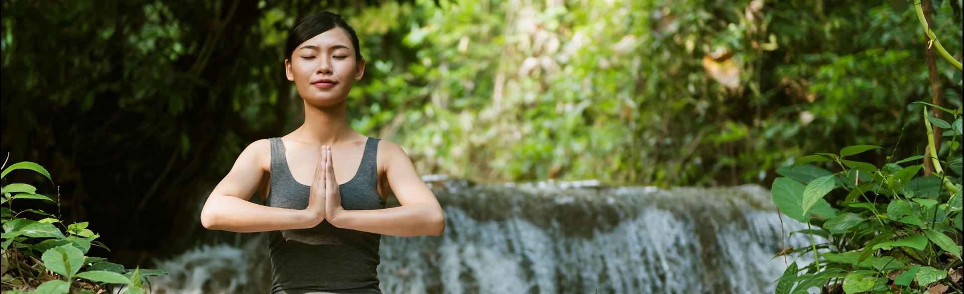 Photo of a young woman meditating while doing yoga near a waterfall.