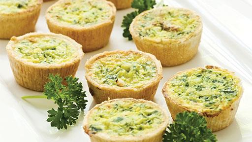 Mini quiches with green filling and parsley on a white surface.