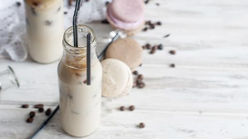 Dairy protein beverages with straws in milk glasses, macaroons, and coffee beans on a white marble surface