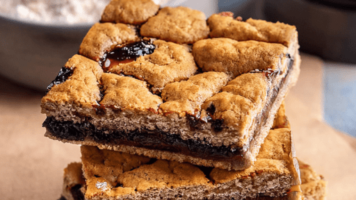 Golden-brown pastry squares with dark filling, stacked in front of a bowl of flour.
