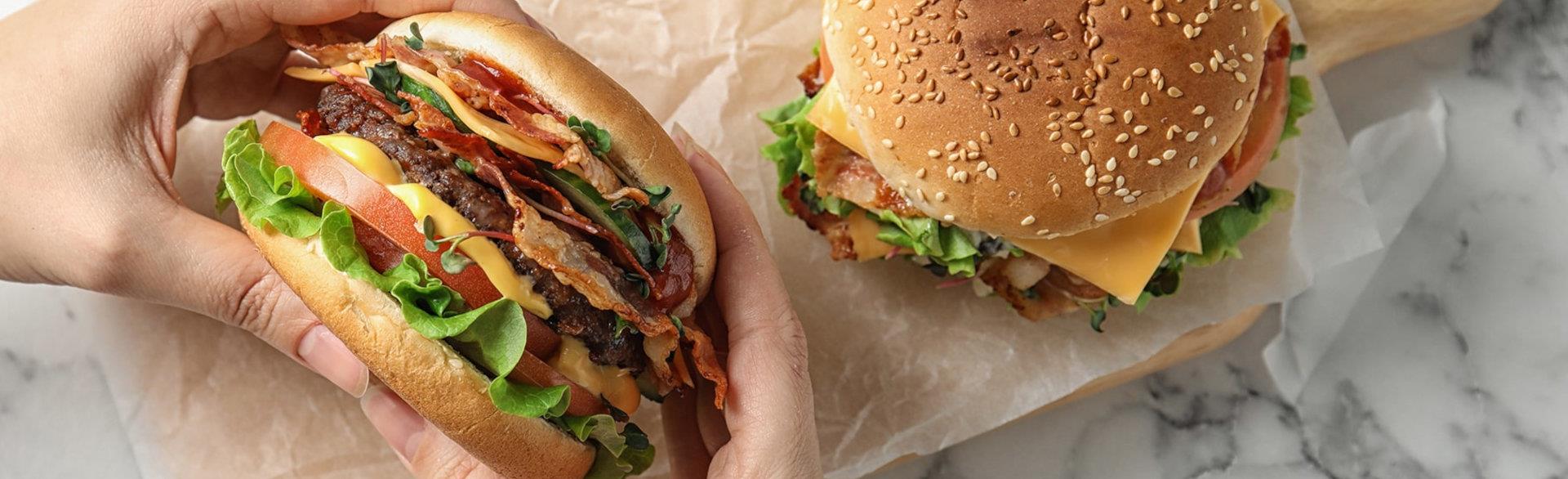 Hands holding hamburger and hamburger on table