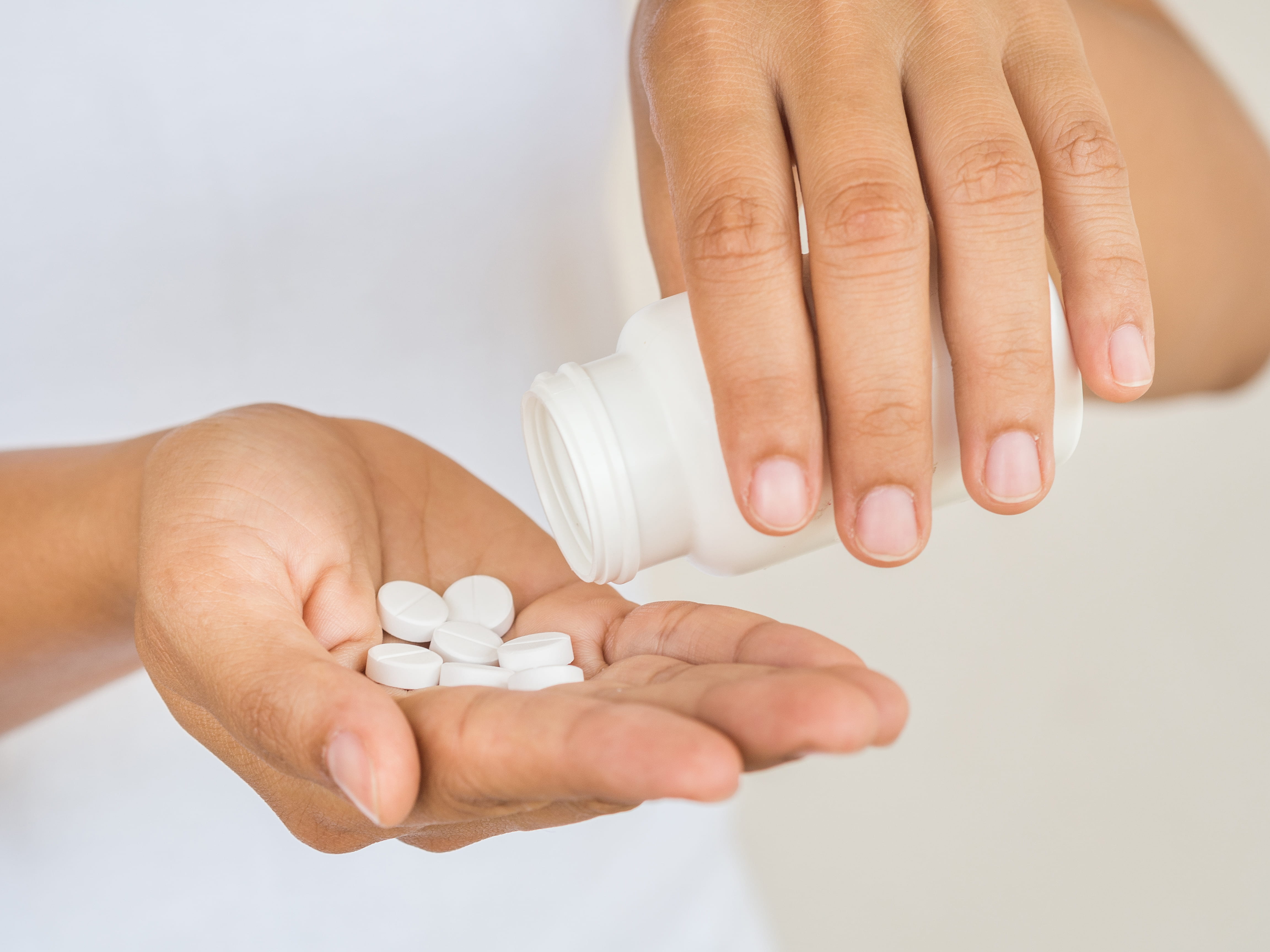 Person pouring white pills from bottle into hand.