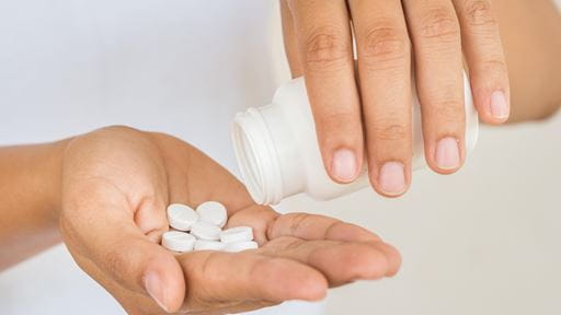 Person pouring white pills from bottle into hand.