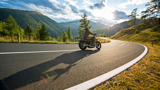 Photo of a motorcyclist riding down a paved highway on a sunny day.