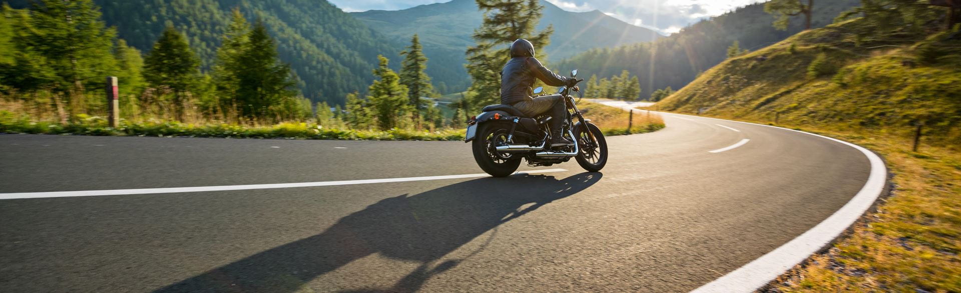 Photo of a motorcyclist riding down a paved highway on a sunny day.