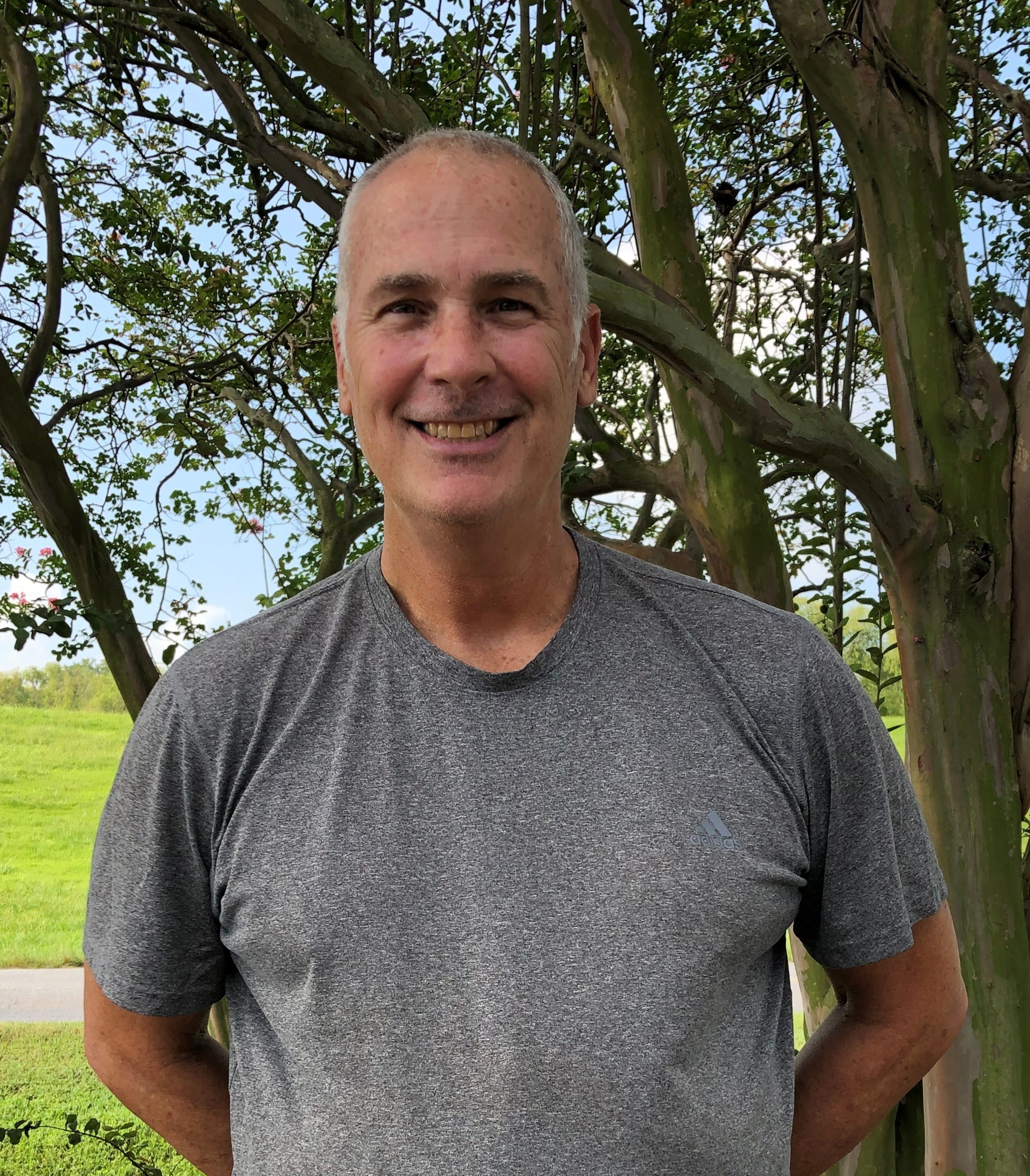 Person standing outdoors in front of a tree, wearing a gray t-shirt.