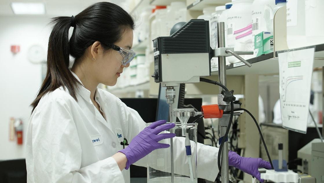 Person in a lab coat and gloves working with equipment in a laboratory.