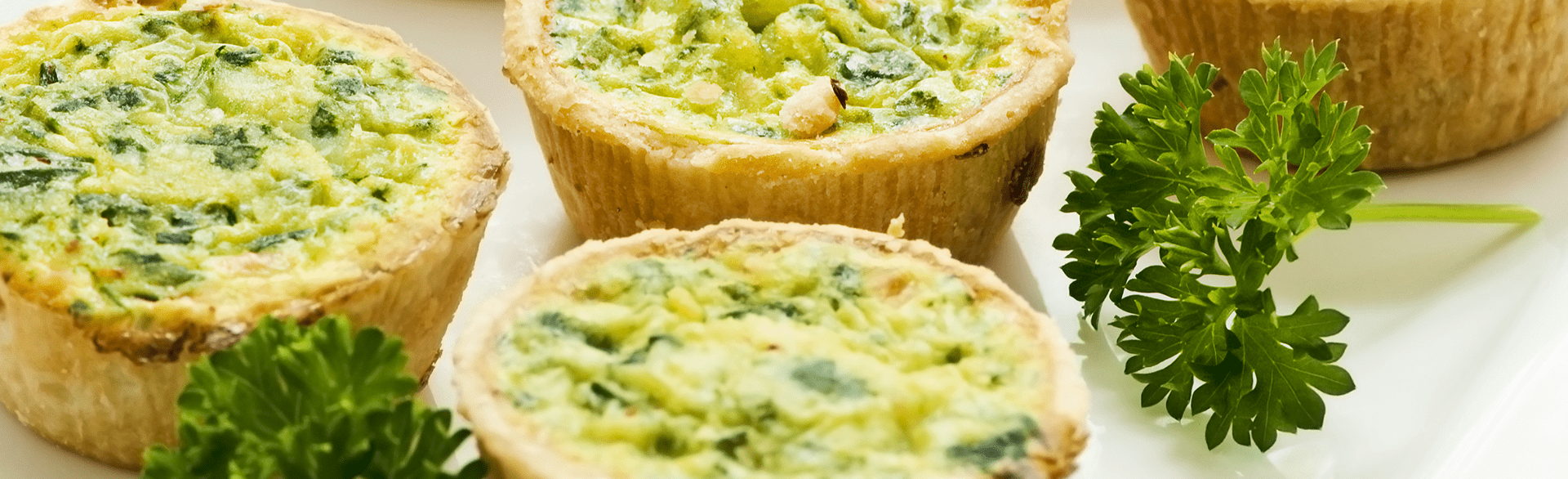 Mini quiches with parsley garnish on a white plate