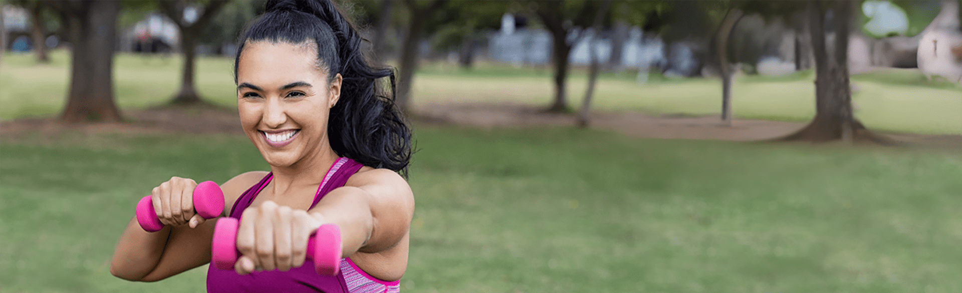 A woman exercising with weights in a park.