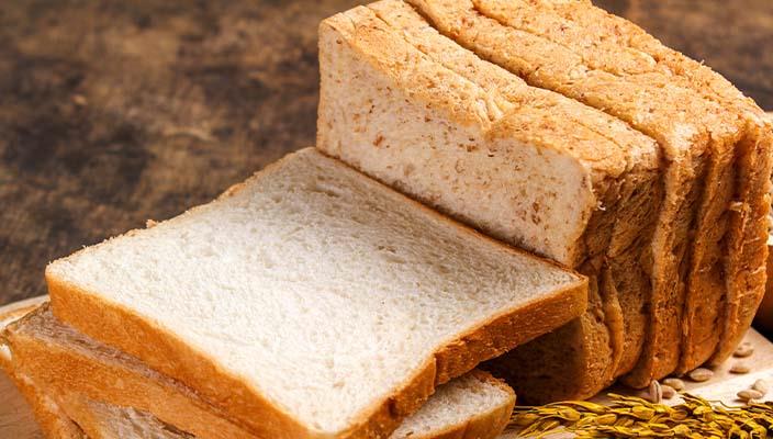 Sliced loaf of mixed white and whole grain bread with seeds scattered around.