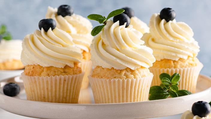 Cupcakes with white frosting, blueberries, and mint leaves on a white plate.