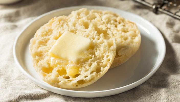 English muffin with melting butter on a white plate.