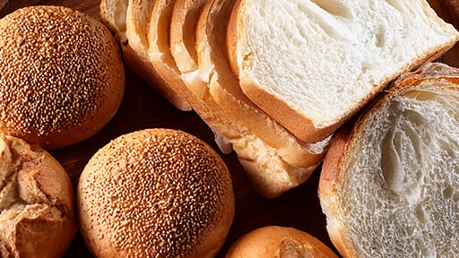 Assorted bread rolls and sliced white bread on a wooden surface.