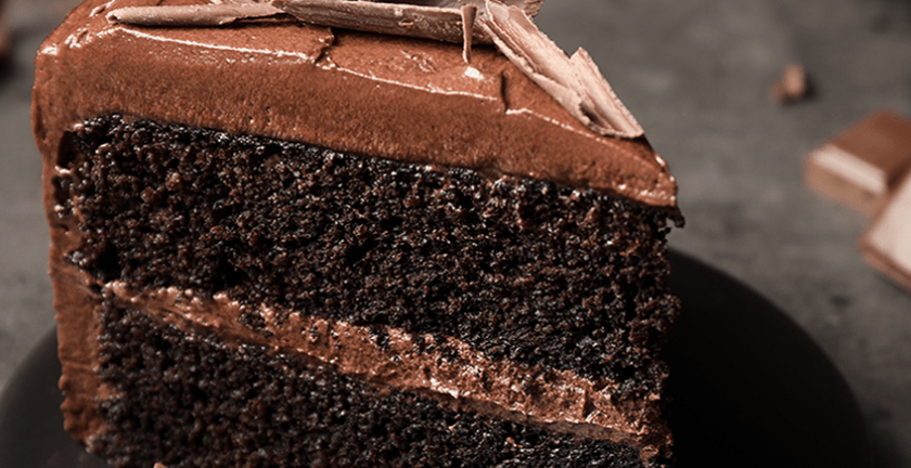 Slice of layered chocolate cake with frosting and shavings on a black plate