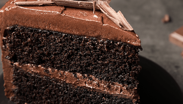 Slice of layered chocolate cake with frosting and shavings on a black plate