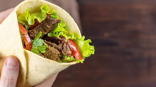 Close-up of a wrap sandwich with lettuce, tomatoes, and grilled meat on a wooden surface