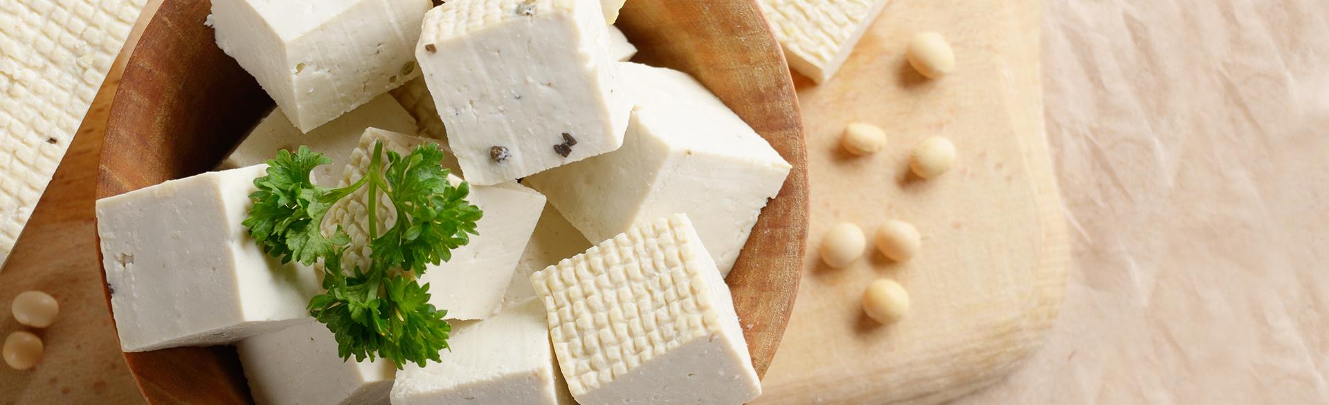 Wooden bowl of tofu cubes with parsley garnish and soybeans nearby