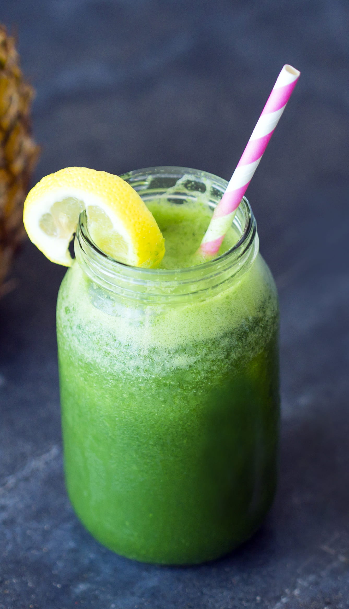 Green smoothie in a jar with a striped straw and lemon slice on a dark surface