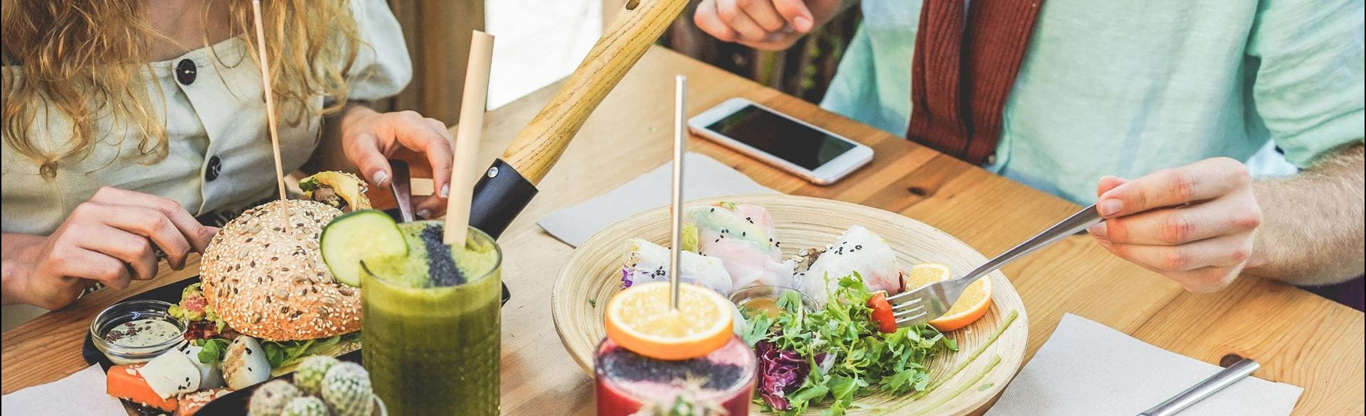 Casual dining table with burgers, salads, drinks, and two people eating