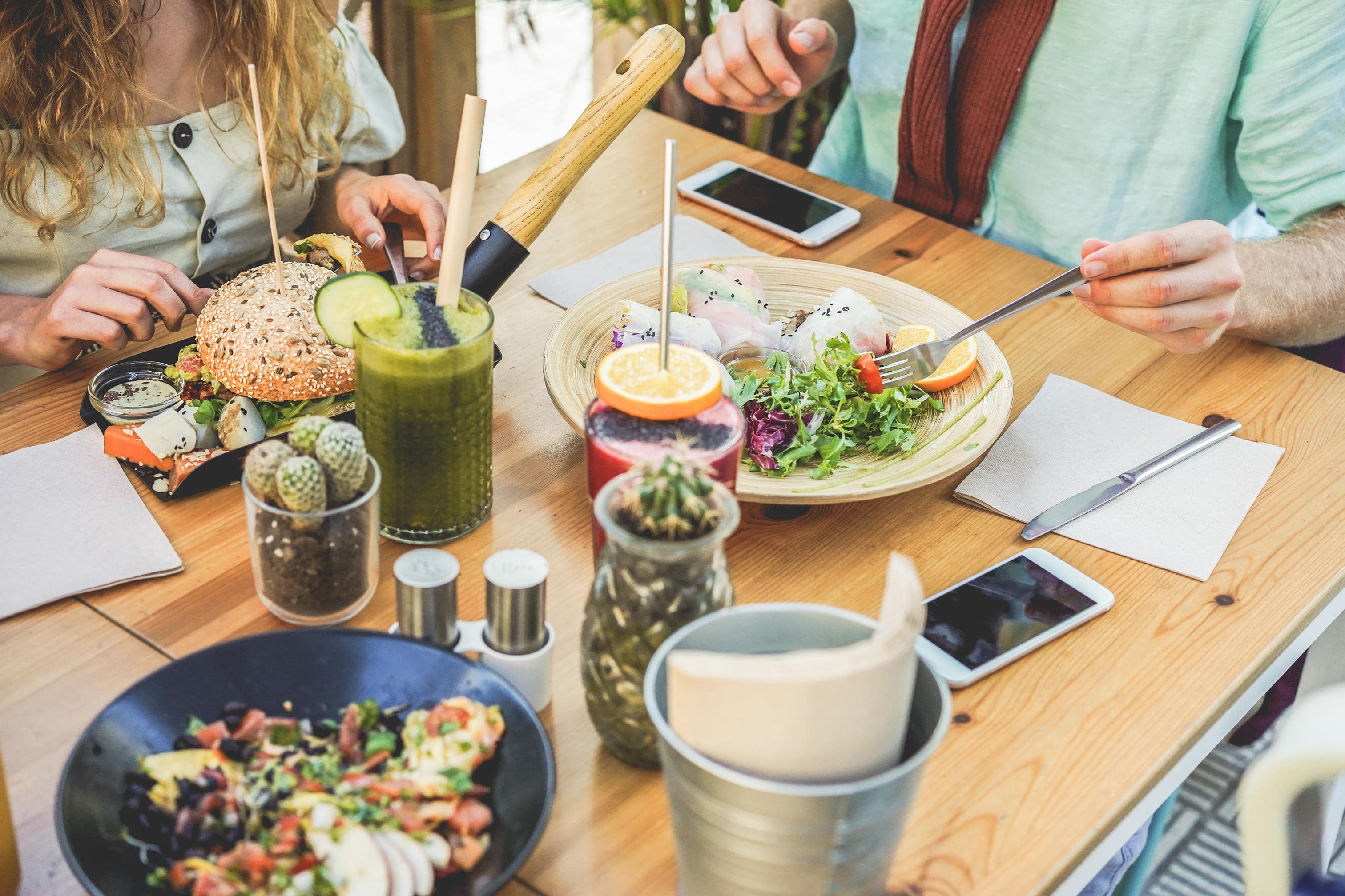 Casual dining table with burgers, salads, drinks, and two people eating