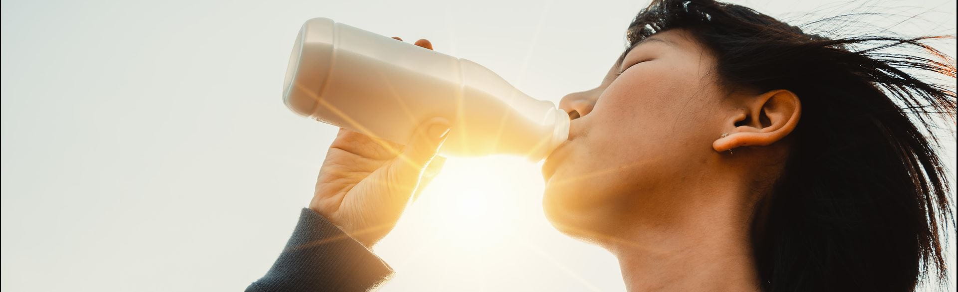 Person drinking from a bottle with sunlight in the background