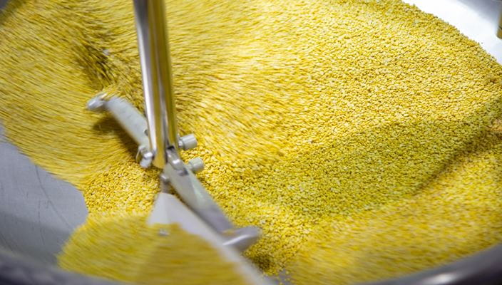 Close-up of a machine mixing yellow grains or pellets in a circular metal container
