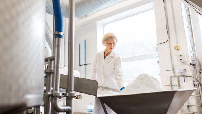 Person in a lab coat working near a large container of white powder in an industrial setting