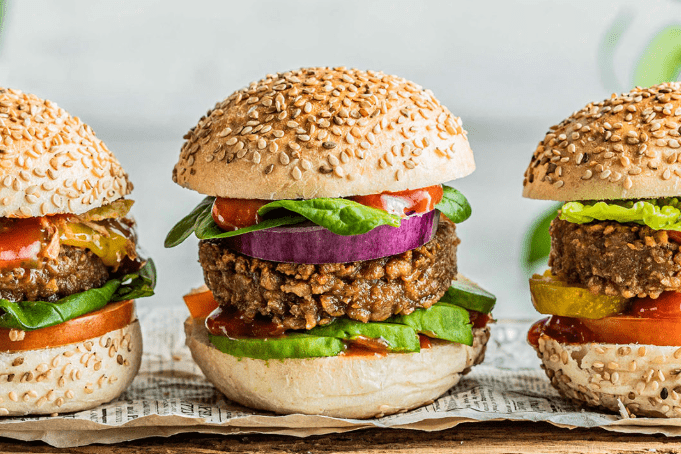 Three veggie burgers with grain patties, avocado, tomato, onion, and lettuce on sesame seed buns
