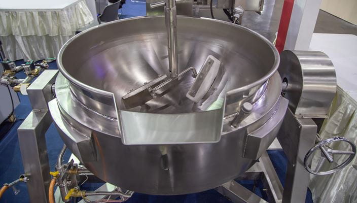 Industrial stainless steel mixing bowl with attachments and connected pipes.