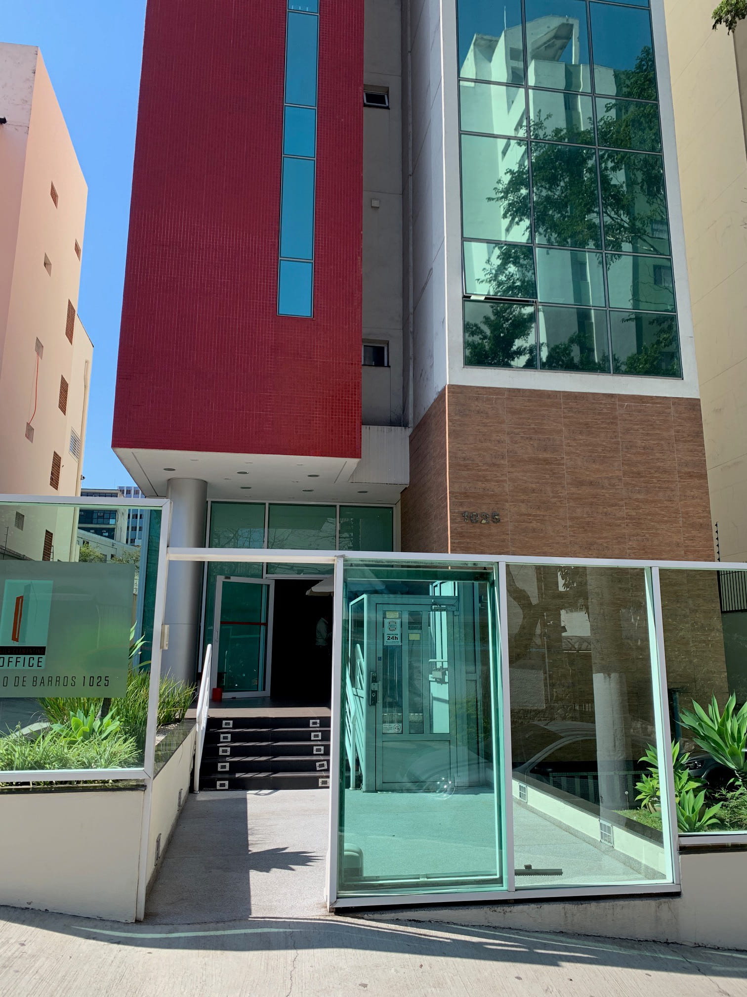 Modern building entrance with glass doors, red and brown facade, and plants by the stairs.