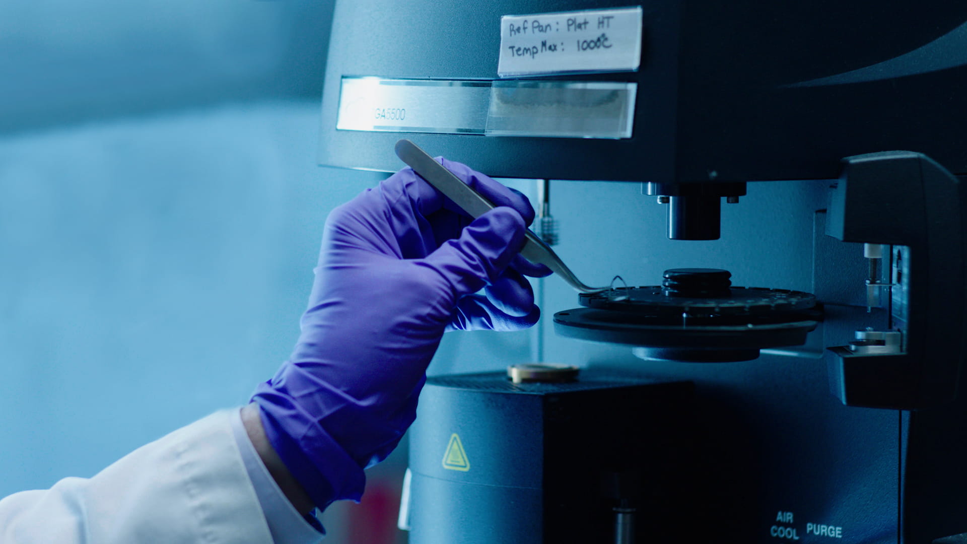 Gloved hand using tweezers on a laboratory instrument