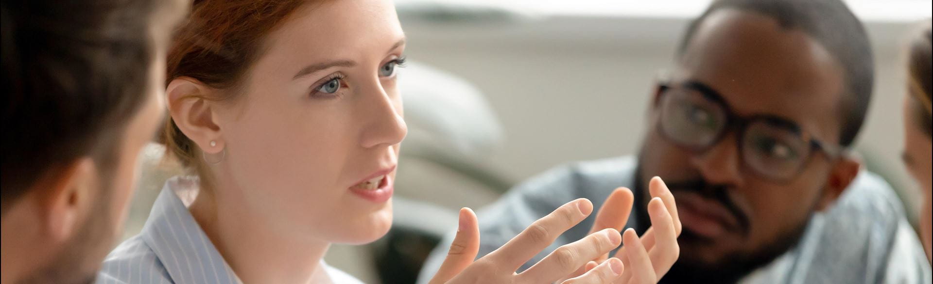Photo of a woman speaking to her colleagues during a meeting.