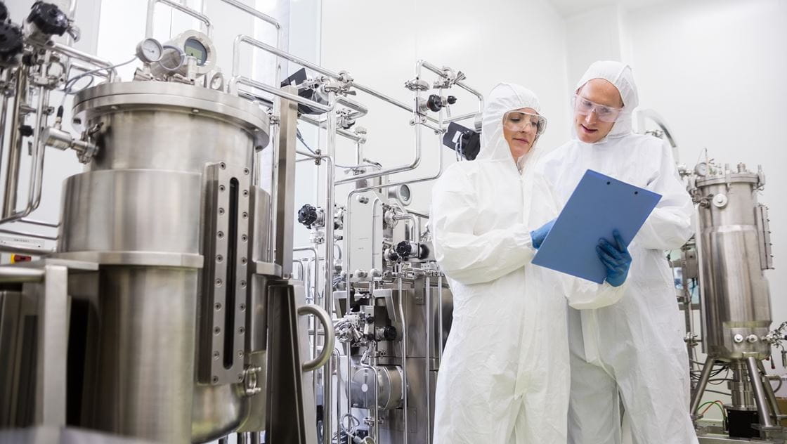 Photo of two scientists in a laboratory reviewing information on a clipboard.